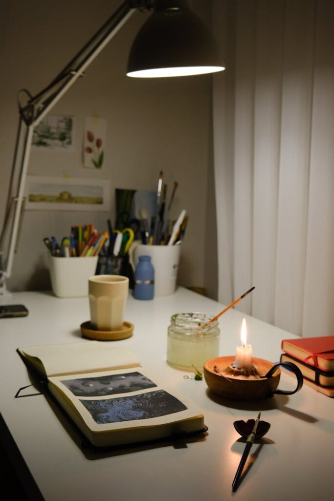 Warm and inviting home office desk setup with journal, candle, and lamp.